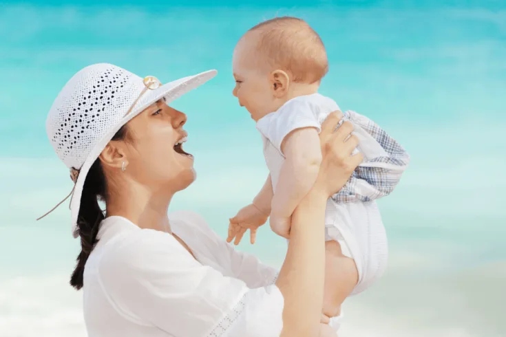 mom in white holding up baby at beach