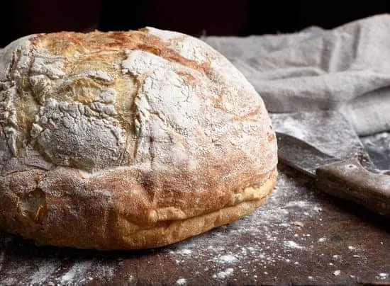baked round white wheat bread on brown old wooden board, close up