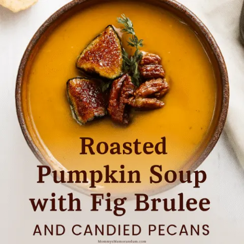 A rustic ceramic bowl of roasted pumpkin soup topped with br&ucirc;l&eacute;ed fig quarters, candied pecans, and a sprig of thyme. The soup has a rich golden-orange hue and is styled on a white wooden surface with a beige linen napkin and crusty bread in the background&mdash;evoking cozy fall vibes and upscale seasonal dining.