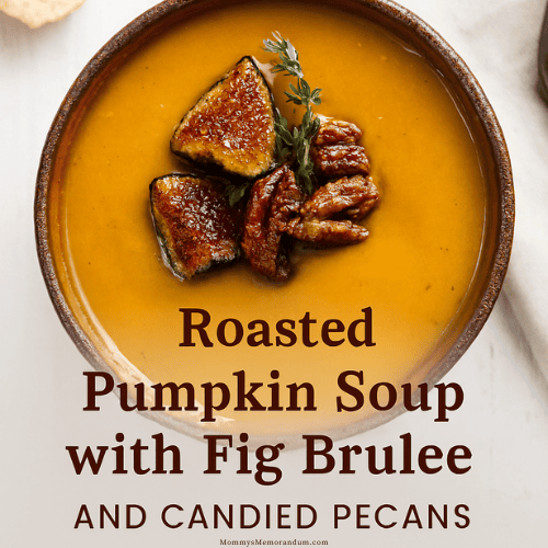 A rustic ceramic bowl of roasted pumpkin soup topped with brûléed fig quarters, candied pecans, and a sprig of thyme. The soup has a rich golden-orange hue and is styled on a white wooden surface with a beige linen napkin and crusty bread in the background—evoking cozy fall vibes and upscale seasonal dining.