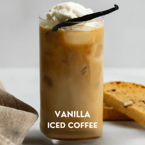 A tall glass of vanilla iced coffee with creamy swirls, topped with whipped cream and a vanilla bean, set against a bright kitchen background with a biscotti and napkin nearby. Text overlay reads &ldquo;Vanilla Iced Coffee &ndash; Better Than Your Barista&rsquo;s Best&rdquo; and &ldquo;Your new morning ritual&mdash;no drive through required.&rdquo;