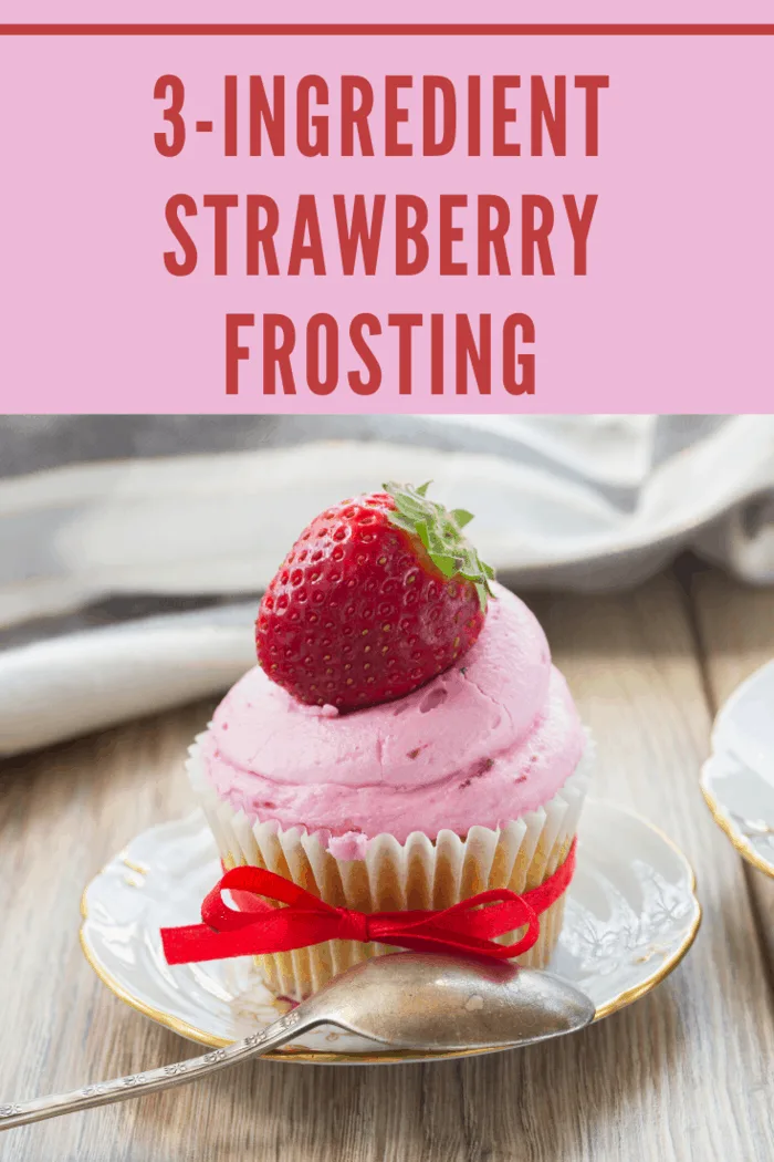 whipped strawberry frosting on a vanilla cupcake and garnished with a ripe strawberry on type and red ribbon around cupcakewrapper