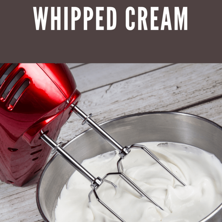 A mixing bowl filled with freshly whipped cream and an electric mixer with red housing.