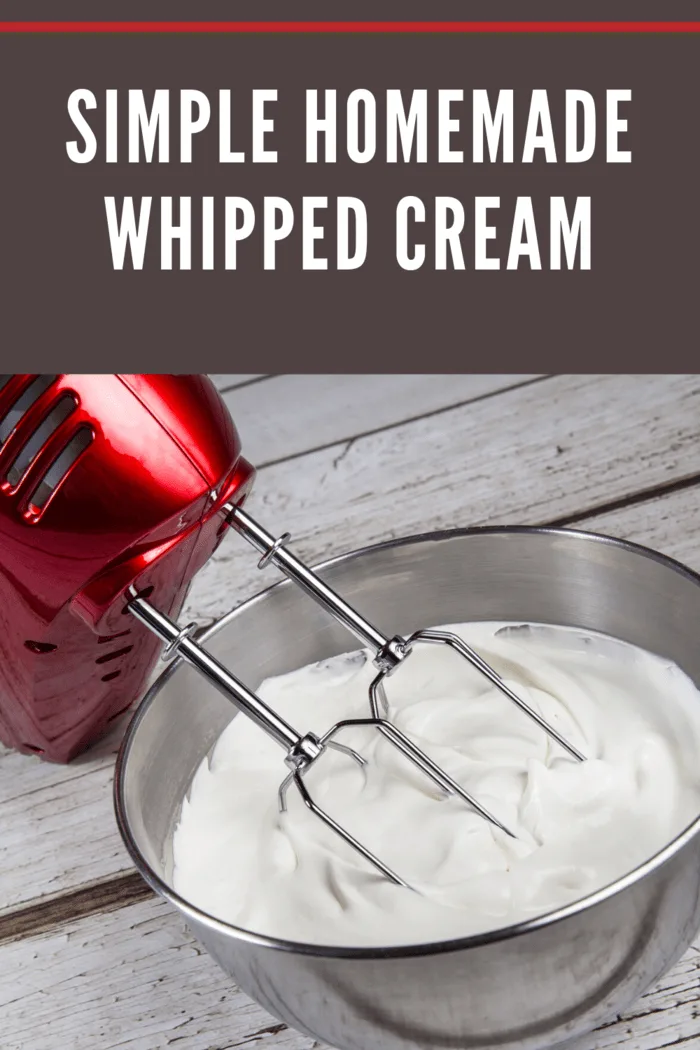 A mixing bowl filled with freshly whipped cream and an electric mixer with red housing.
