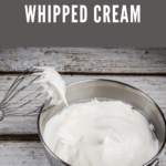 A mixing bowl filled with freshly whipped cream and a whisk covered in whipped cream.