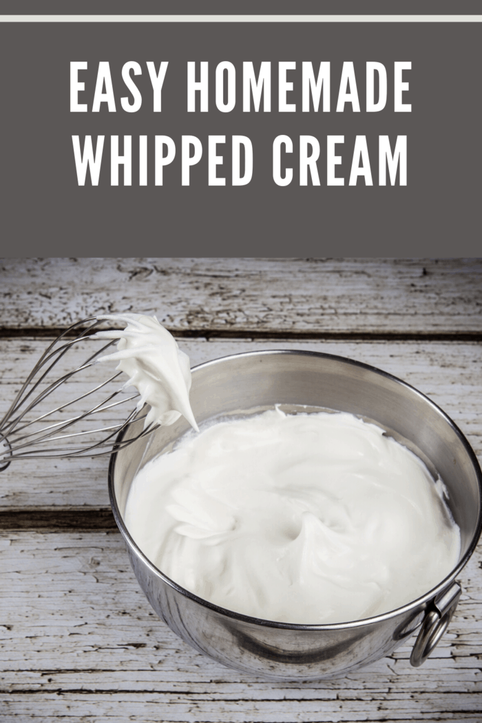 A mixing bowl filled with freshly whipped cream and a whisk covered in whipped cream.