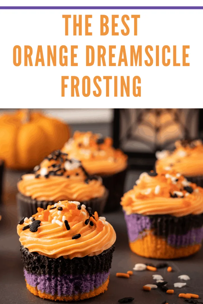 Halloween cupcakes with purple, black and orange cake bottom frosted with a swirled orange creamsicle frosting. Cupcakes are decorated with Halloween themed sprinkles, bats , ghosts and multi colored sprinkles. A pumpkin and spider web lantern can be seen in the bac
