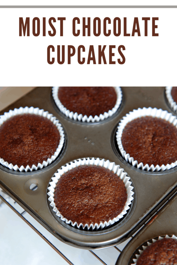 moist chocolate cupcakes in cupcake tins cooling on wiring rack
