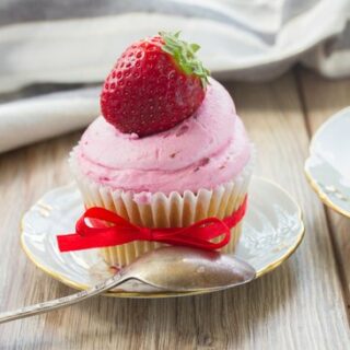 Cupcake with fluffy pink 3-ingredient strawberry frosting topped with a fresh strawberry on a saucer.