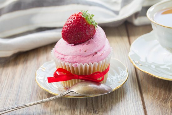 Cupcake with fluffy pink 3-ingredient strawberry frosting topped with a fresh strawberry on a saucer.