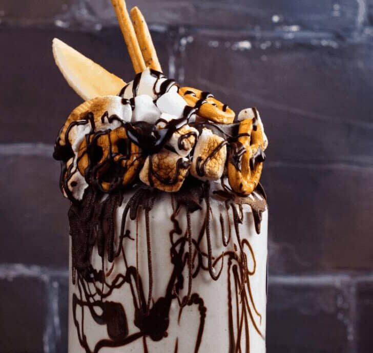 toasted marhmallow milkshake with pretzel embellisments and chocolate syrup on grunge vintage background.