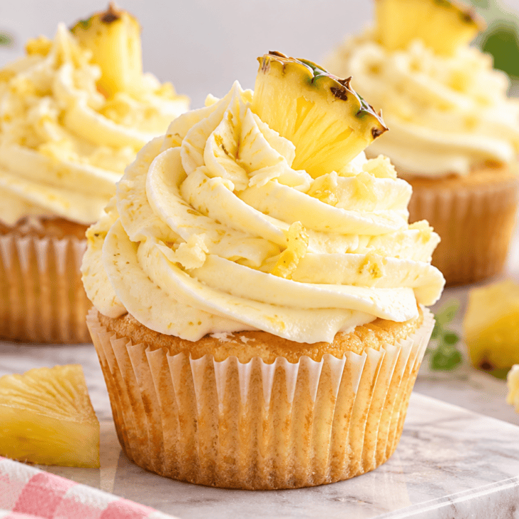 Easy pineapple frosting piped onto vanilla cupcakes with fresh pineapple