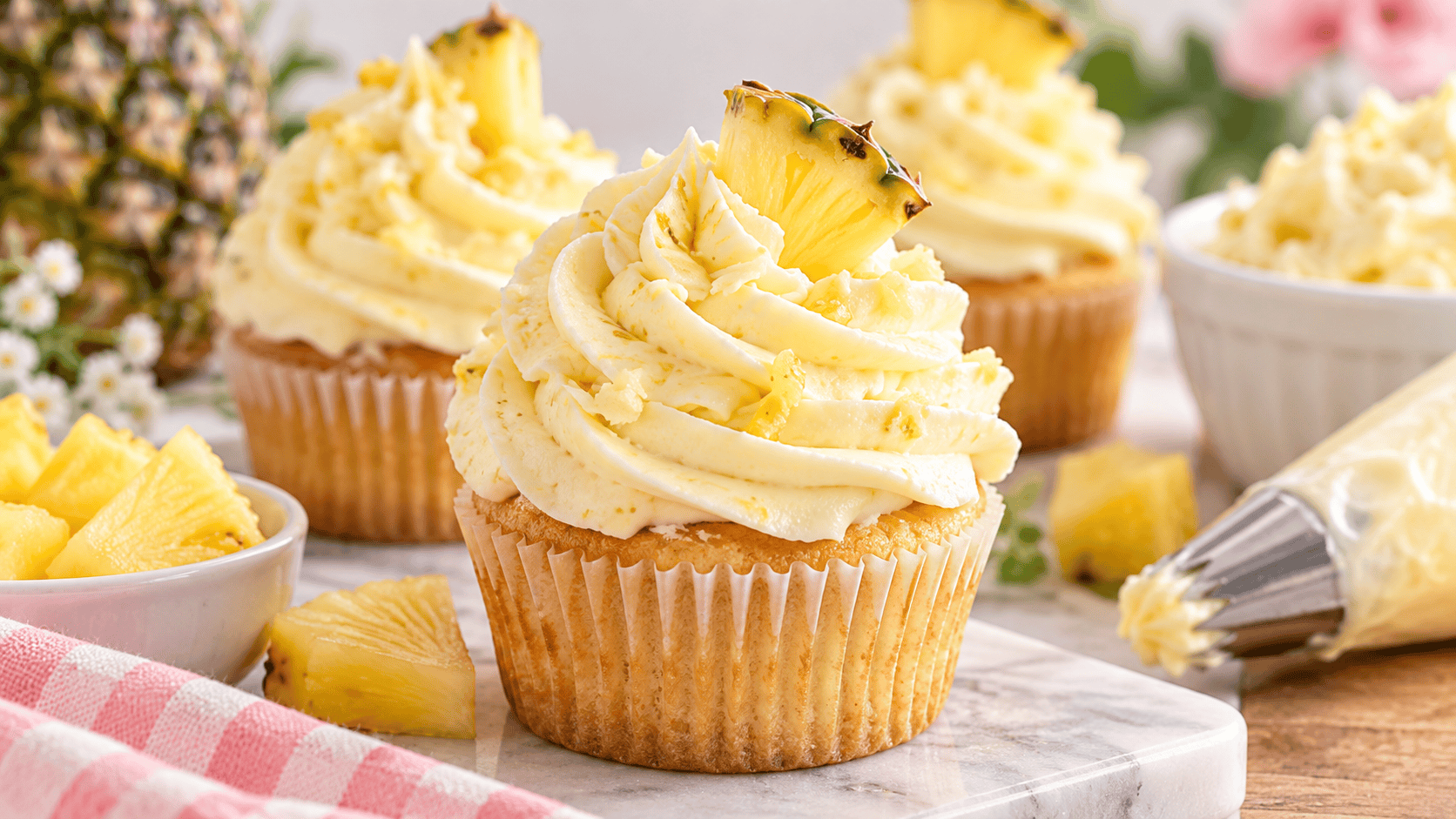 Easy pineapple frosting piped onto vanilla cupcakes with fresh pineapple