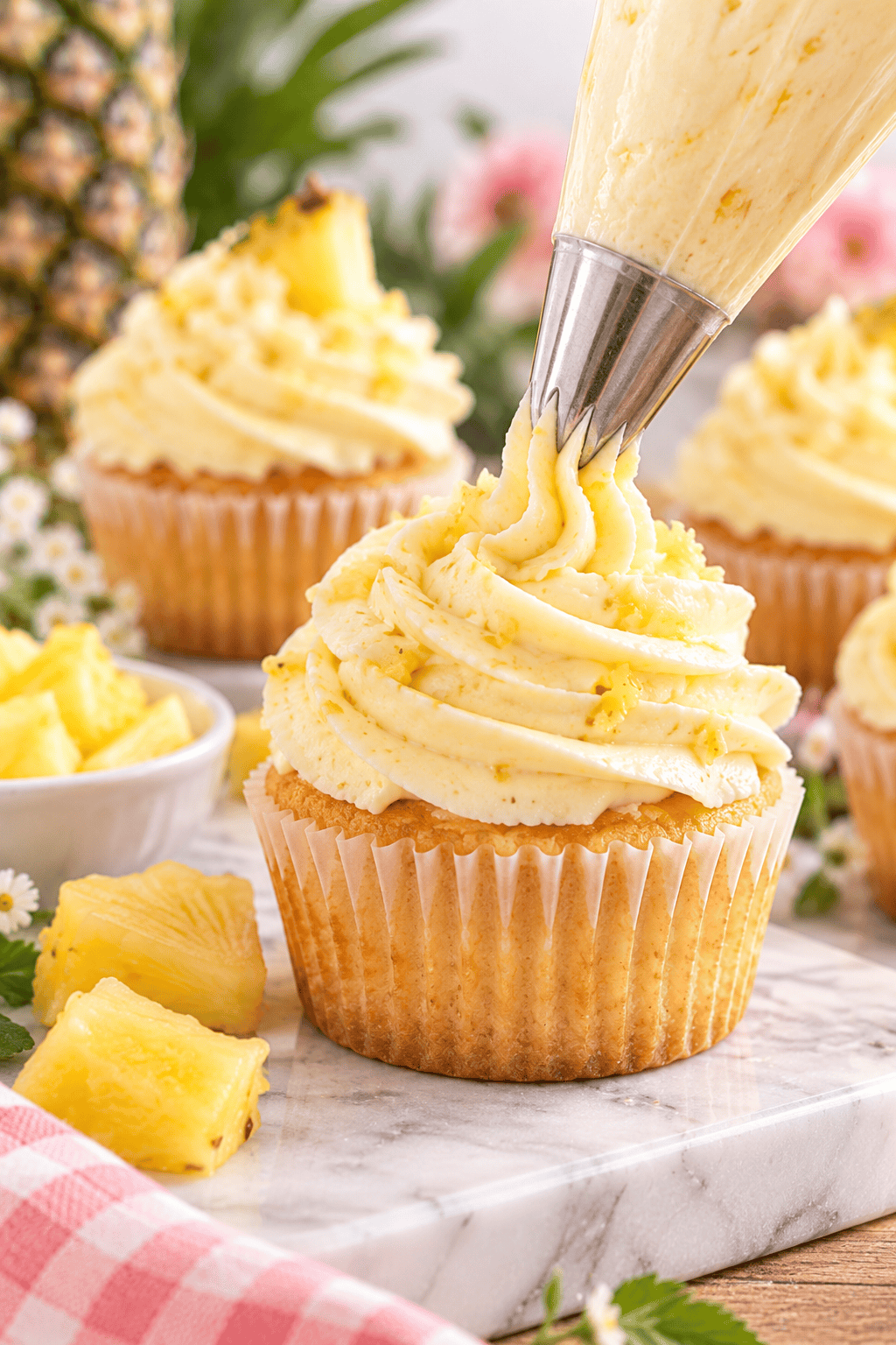 Pineapple cream cheese frosting being piped onto a vanilla cupcake