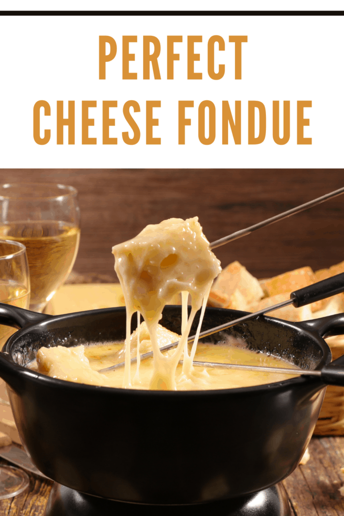 Cheese fondue in black fondue pot with bread pieces on skewers being dipped