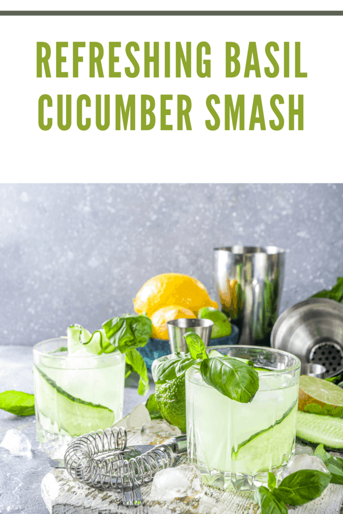 two basil cucumber smash cocktails garnished with basil leaves with orange in back