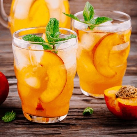 Summer cold drinks: homemade peach sangria with ice cubes, and mint in glass on wooden background.