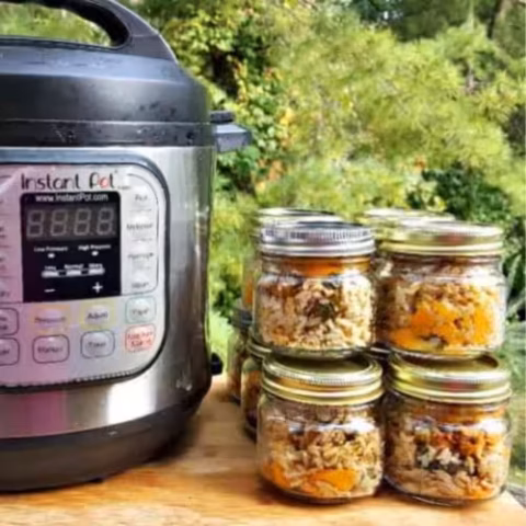 Instant Pot and jars of homemade dog food on a wooden table outdoors, ready for storage.