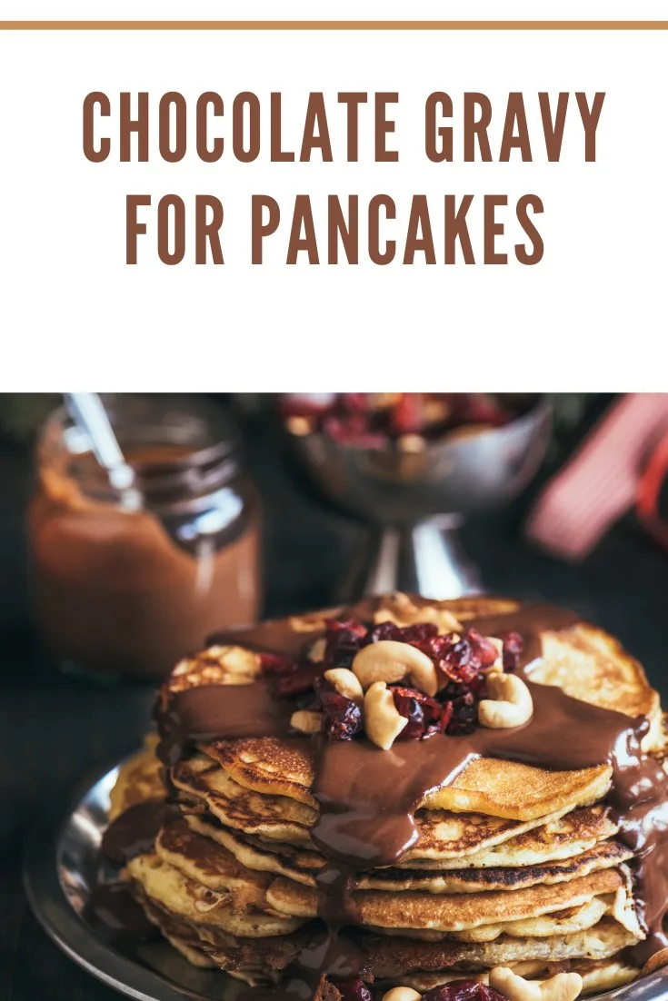 A stack of pancakes topped with chocolate gravy, nuts, and dried fruit, with a jar of chocolate sauce in the background.