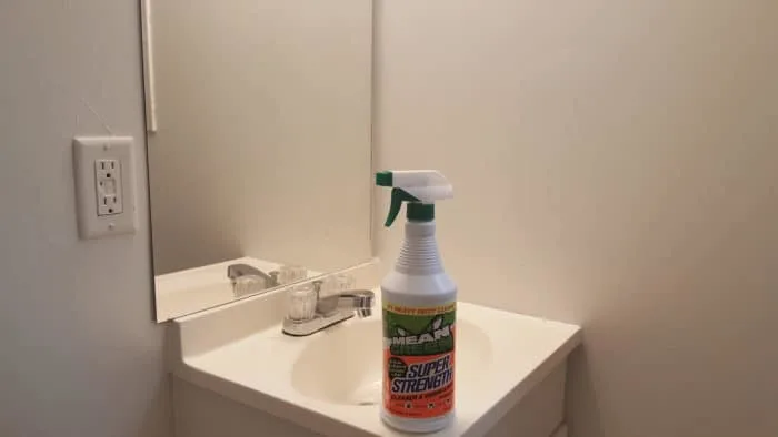 A bottle of Mean Green Super Strength Cleaner on a white bathroom sink counter next to a mirror.