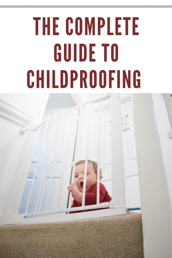 Baby boy on the landing of his home. He is behind a baby safety gate that is stopping him from the danger of the staircase.