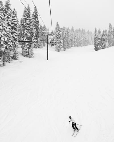 black and white of snow falling on ski run where lone skiier is skiing