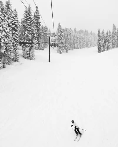 black and white of snow falling on ski run where lone skiier is skiing