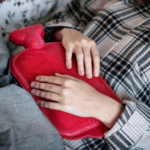 woman in plaid shirt laying down with red heating pad on stomach