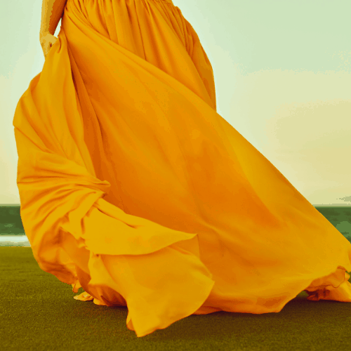 unrecognizable woman in summer time with yellow chiffon dress flying all around.