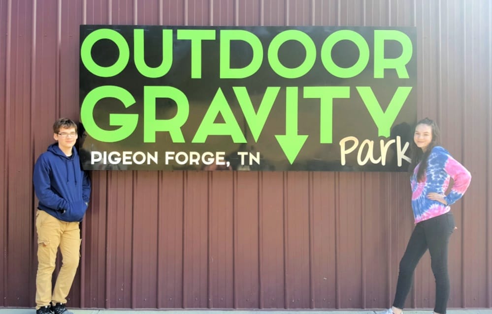 Two kids posing by the Outdoor Gravity Park sign in Pigeon Forge, TN, ready for an adventure