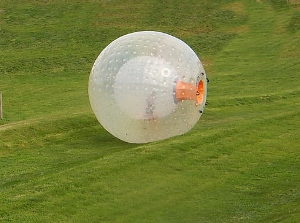 A person inside a large zorbing ball rolling down a grassy hill at Outdoor Gravity Park in Pigeon Forge, TN