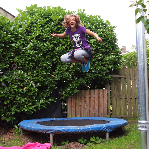 girl jumping on trampoline in backyard