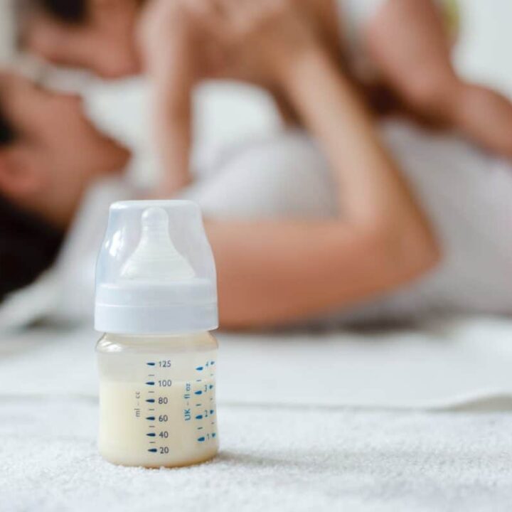 baby bottle with milk in focus with mother and baby out of focus in background