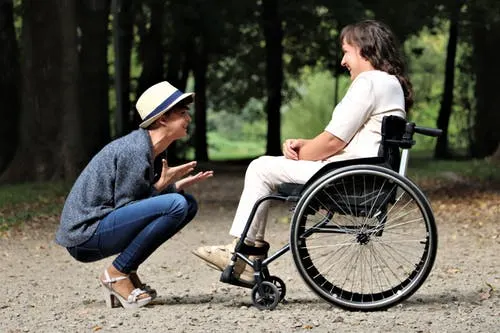 woman sitting in wheelchair with woman bending down to talk to her