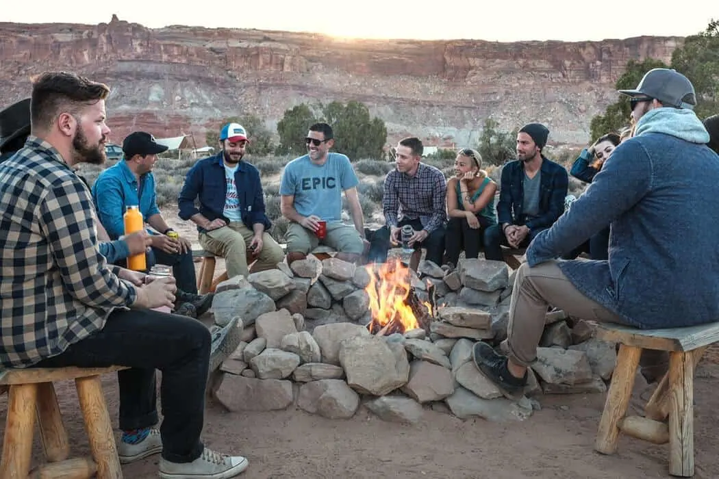 group of adults gathered around a camp fire with cliff mountains behind them