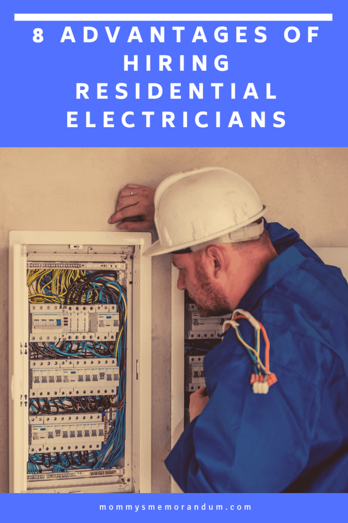 A professional electrician in a blue uniform and white helmet inspecting a residential electrical panel