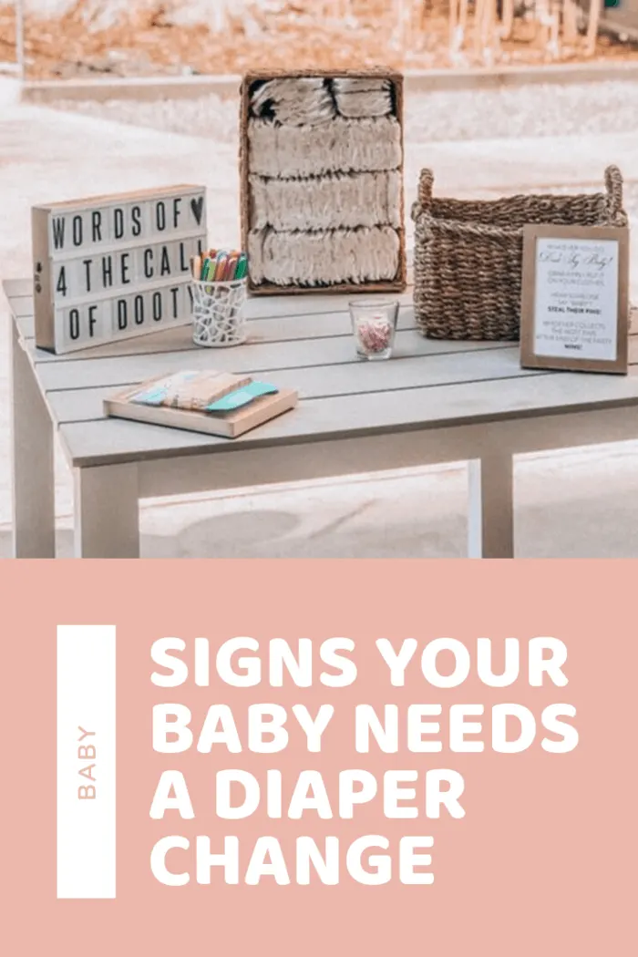 Stylish nursery decor setup on a wooden table featuring a sign that reads 'Signs Your Baby Needs A Diaper Change' among other baby items.