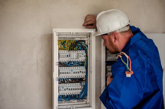 A professional residential electrician in a blue uniform and white helmet inspecting a residential electrical panel