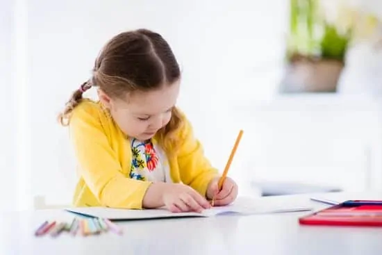 Preschool girl practicing writing, reading, and coloring at home, developing essential creative skills