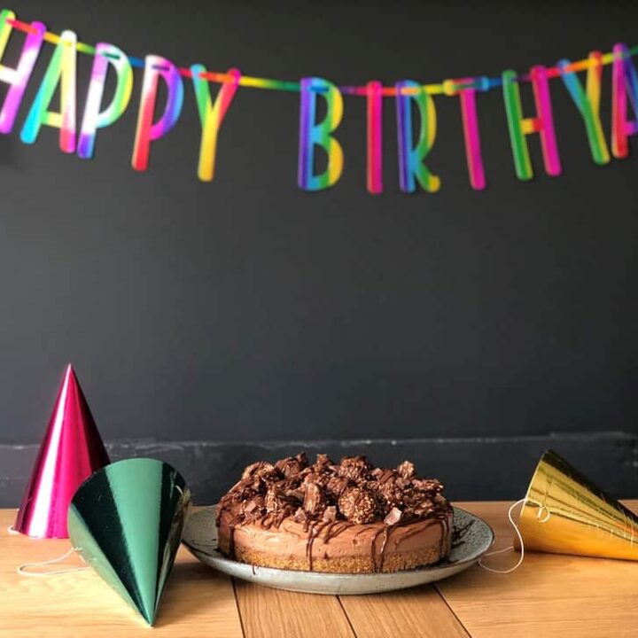 chocolate cake on table with foil hats, black background with rainbow Happy Birthyay banner