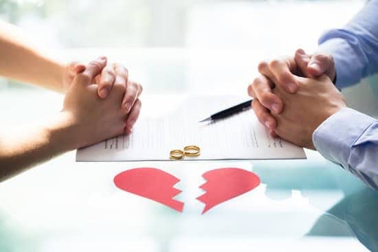 man and woman sitting across from each other, hands on table, paper heart broken and wedding rings on table.