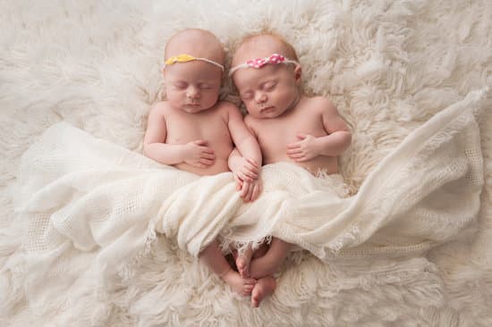 Seven week old fraternal, twin baby girls sleeping on a white flokati rug.