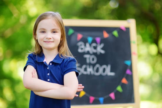 girl starting school standing next to back to school written on chalkboard