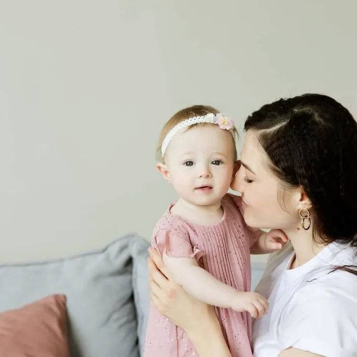 young mother cuddling toddler daughter in mauve dress with matching headband