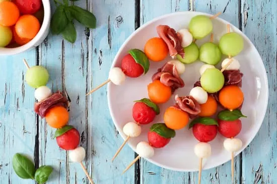 Plate of delicious summer fruit skewers with melon, cheese and prosciutto on a rustic blue wood background