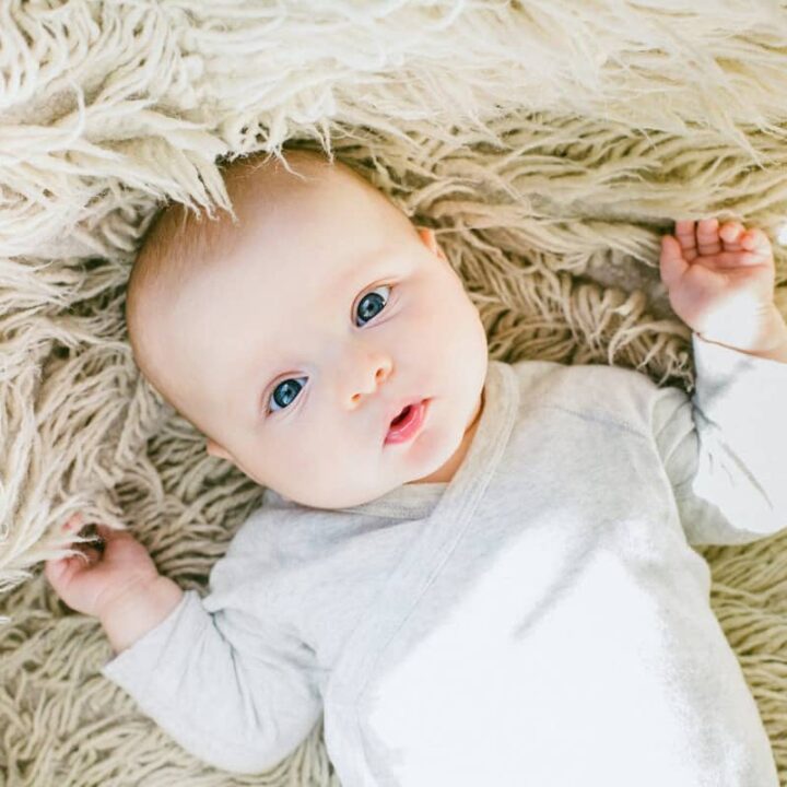 baby with blue eyes laying on beige long haired rug looking up at camera