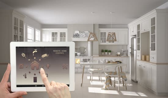 Smart remote home control system on a digital tablet. Device with app icons. Interior of scandinavian white and wooden kitchen in the background, architecture design.