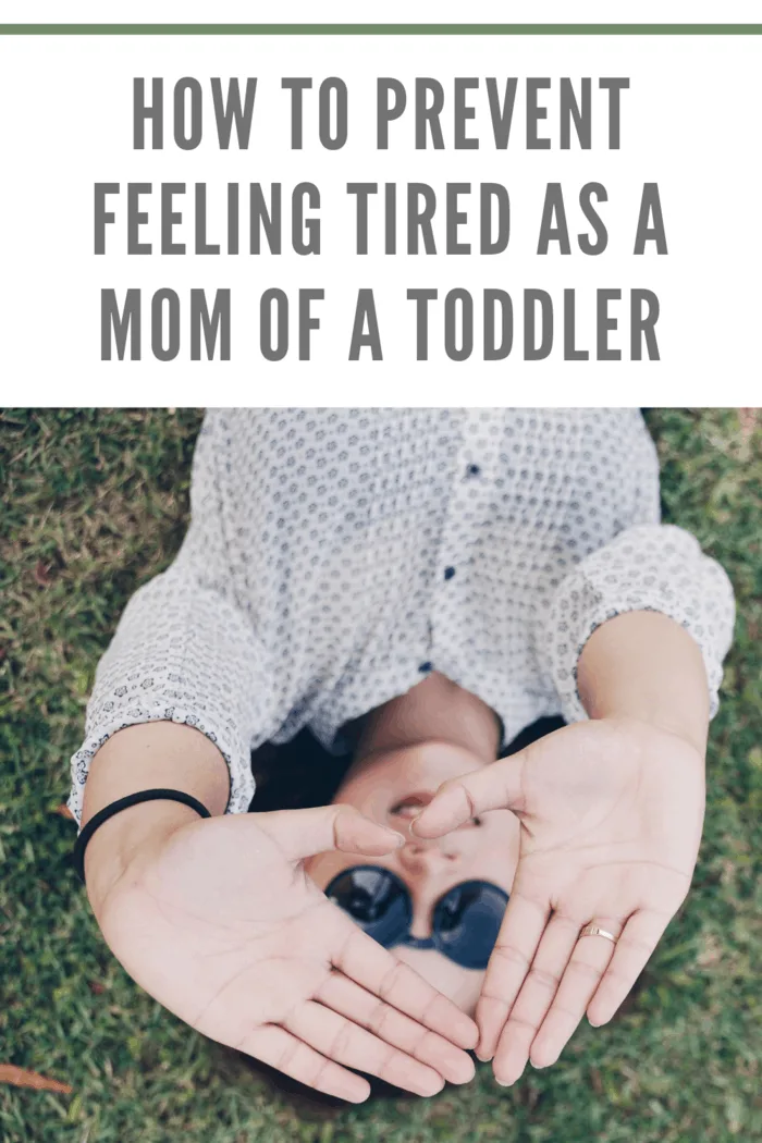 tired mom of a toddler laying on her back on the grass using hands to block the sun