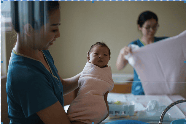 new baby bundled in pink blanket being held up by nurse