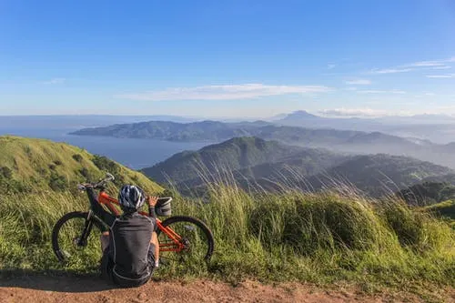 woman resting at top of hill after cycling to enjoy the scenic view of mountains
